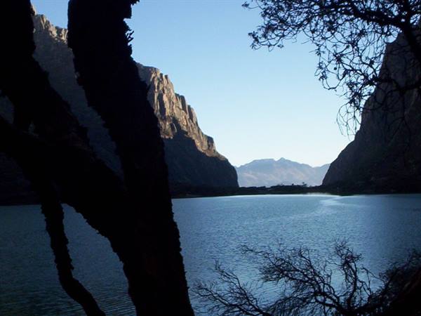 Blue lake framed by dark rock cliffs, silhouetted branches, clear sky