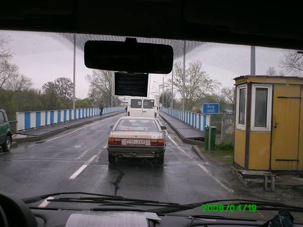 Car queuing on a rain-soaked bridge, yellow toll booth and river sign