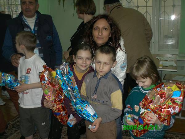 Woman and smiling children indoors holding colorful wrapped gifts