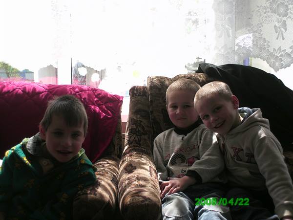 Three smiling children sitting on a floral armchair indoors