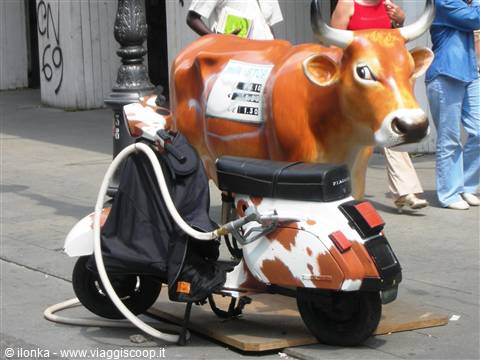 Brown cow sculpture next to a spotted Vespa scooter parked on the street