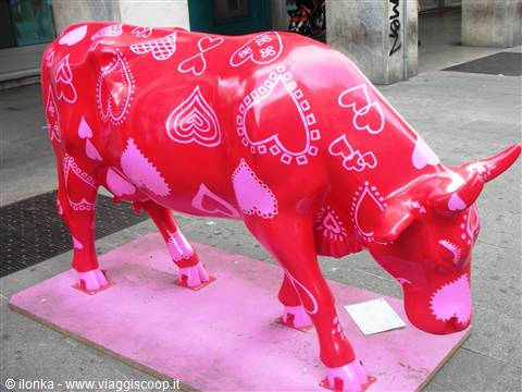 Red painted cow sculpture decorated with hearts, street art installation