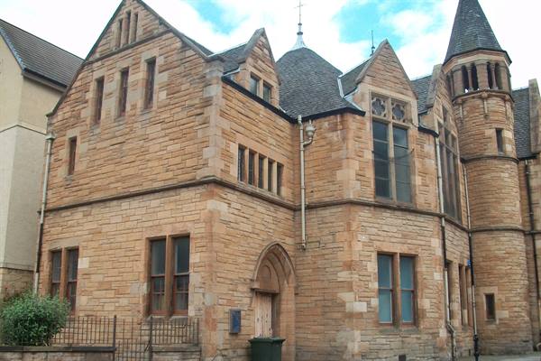 Old sandstone building with Gothic turrets and stained glass under cloudy sky