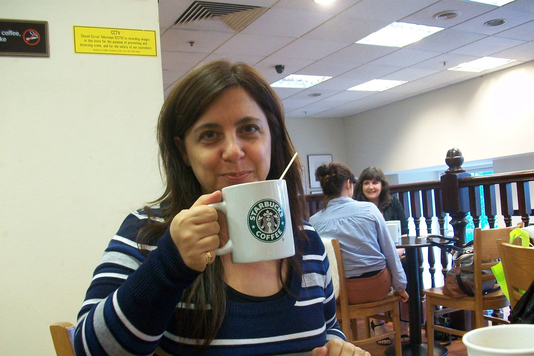 Smiling woman sipping from a large Starbucks mug at the café counter
