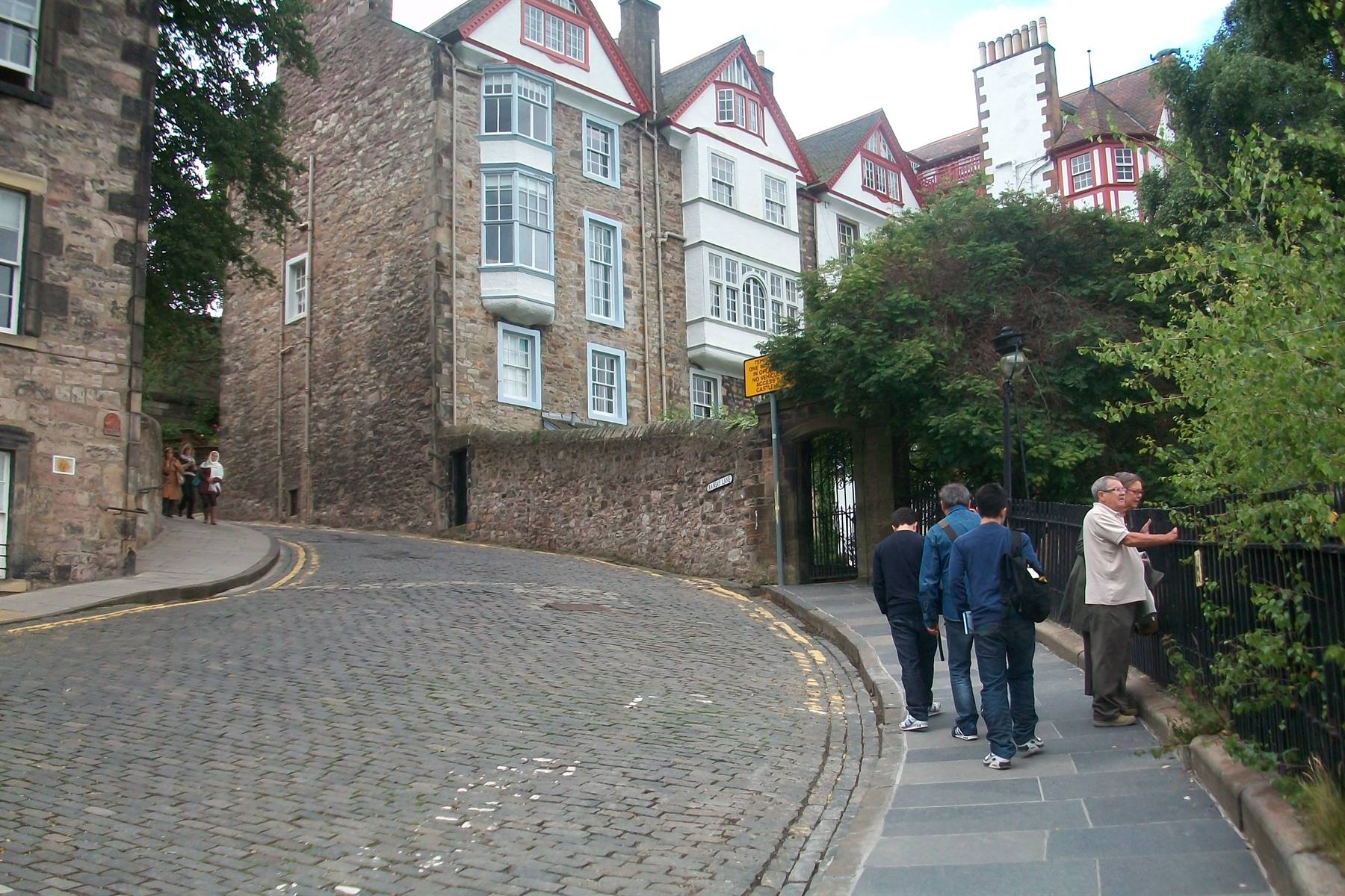 Tourists on a cobbled street beside stone houses with red trim, Edinburgh