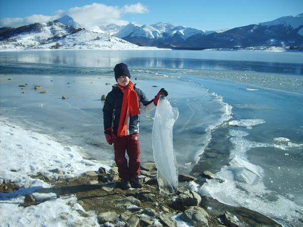 Child in orange scarf lifts a slab of ice on the frozen lake