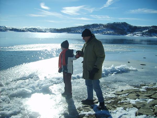Man and child walk along the icy shore of a snowy lake