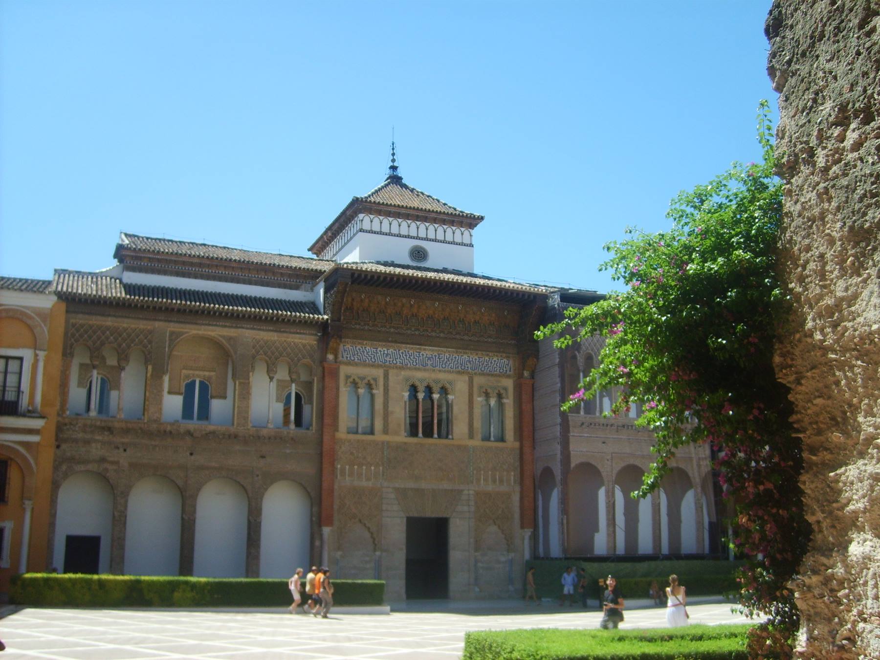 Visitors stroll across the courtyard of Seville's Alcázar under a clear blue sky