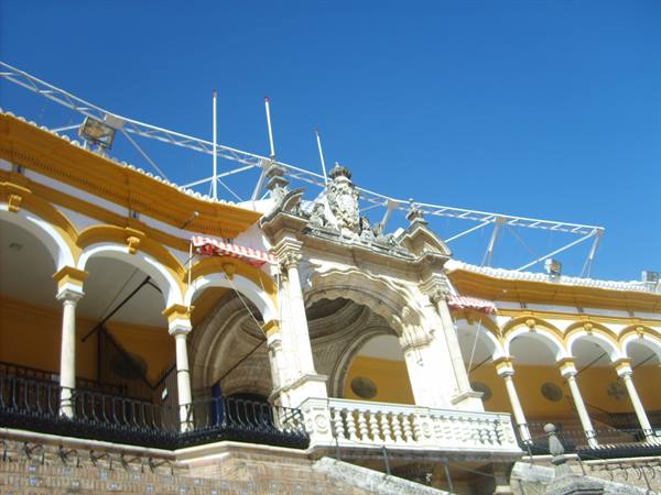Yellow and white arches of Seville's bullring under a blue sky