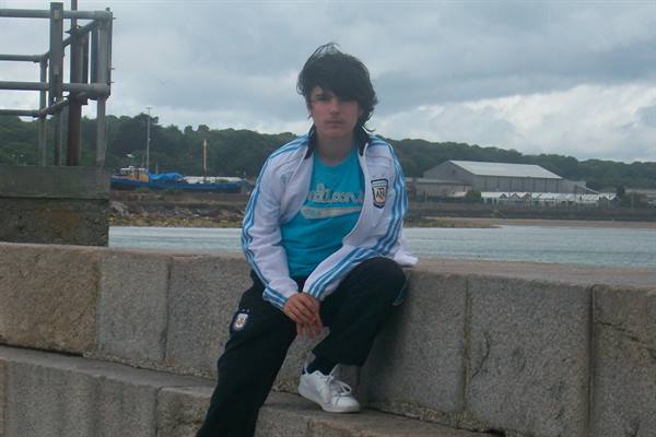 Boy in light blue tracksuit sitting on stone wall by the harbour