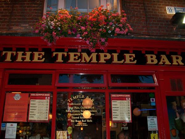 Red facade of the Temple Bar in Dublin, flowers above the sign, lit evening