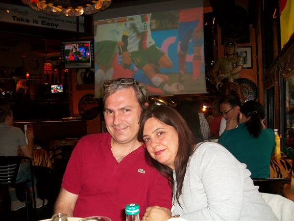 Smiling couple in a sports bar in front of the screen showing a match