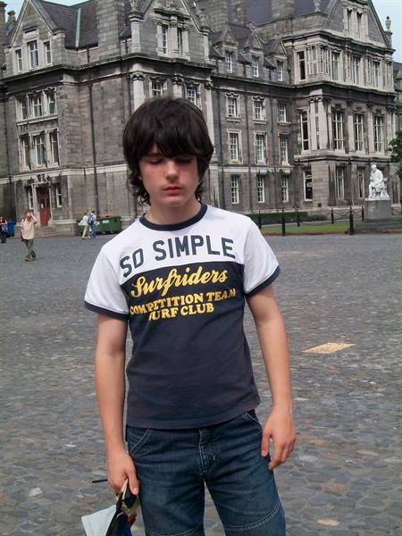 Boy in t-shirt in front of Trinity College Dublin, grey stone, soft light