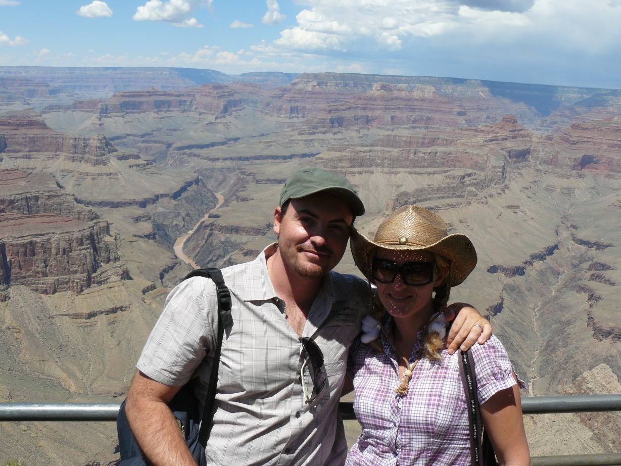 Couple embracing before the Grand Canyon, the Colorado river carving red gorges below clouds
