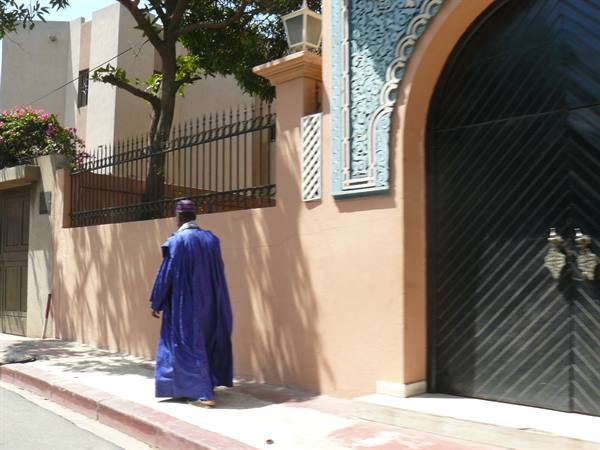 Man in long blue robe walks past pink wall with black arched door