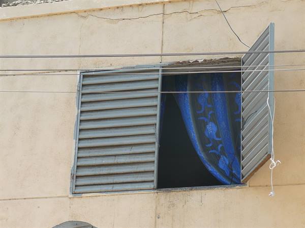 Window with grey metal shutters and blue curtain on beige wall, power lines
