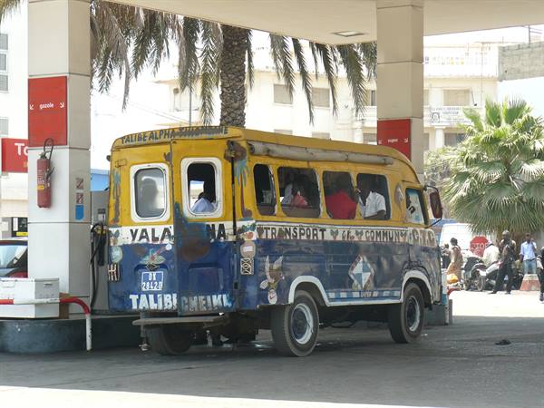 Pulled blue and yellow minibus refueling at a gas station among palm trees