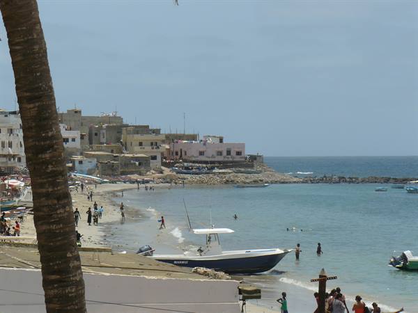 Blue boat moored on the beach, swimmers and colorful houses along the coast