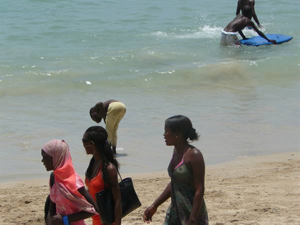 Women walk on the sand while boys play with a bodyboard in the water