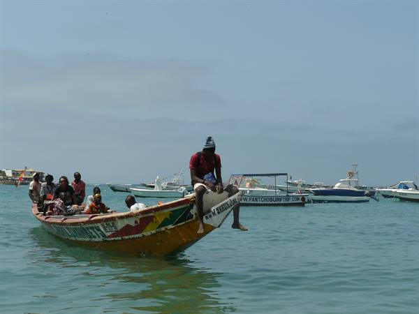 Fishermen on a painted wooden pirogue in a bay with motorboats