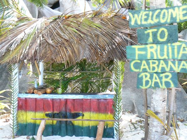 Wooden beach shack with palm-thatch roof, painted Ghana flag, Welcome to Fruita Cabana Bar sign