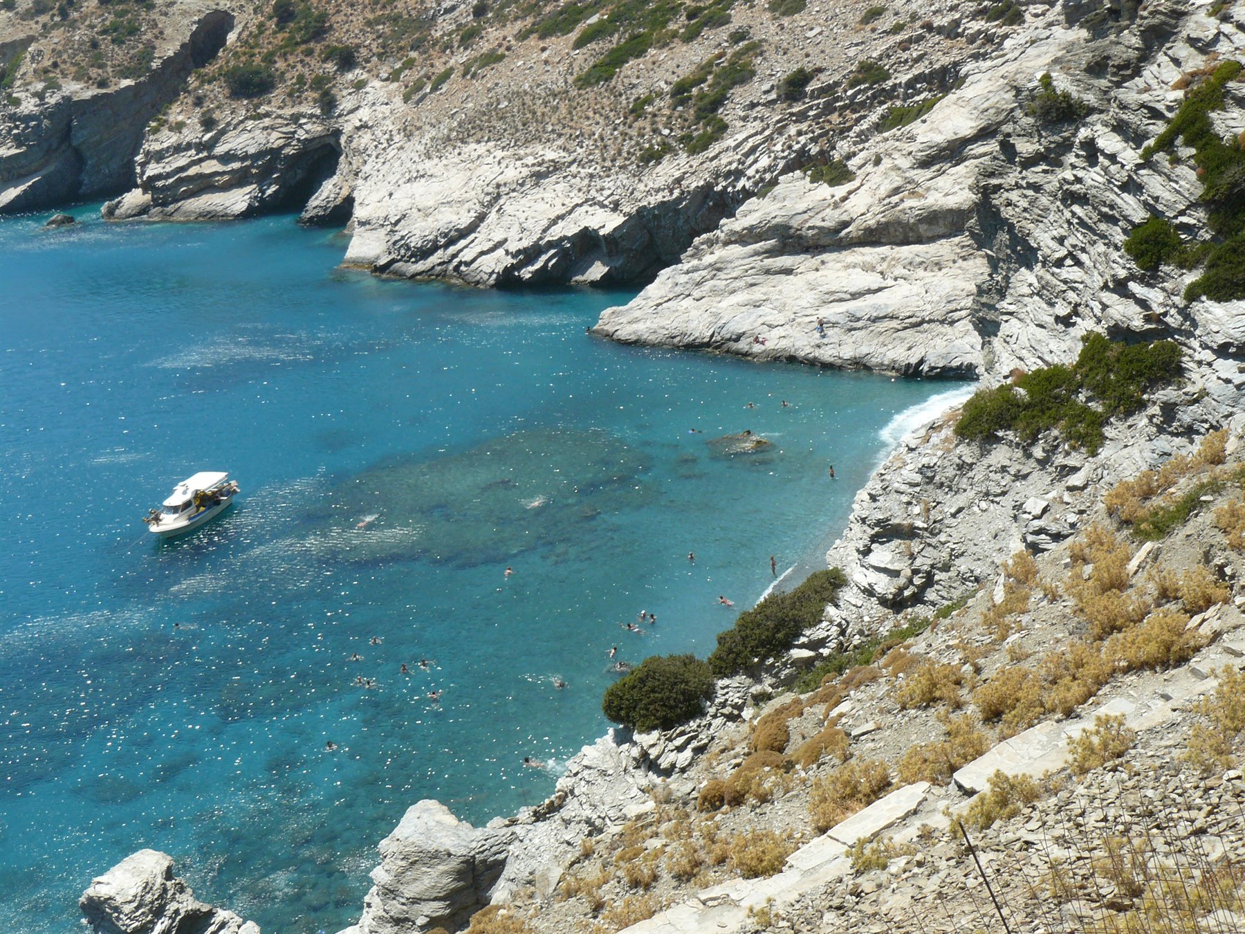 barca ferma in baia rocciosa, acqua turchese, bagnanti tra gli scogli