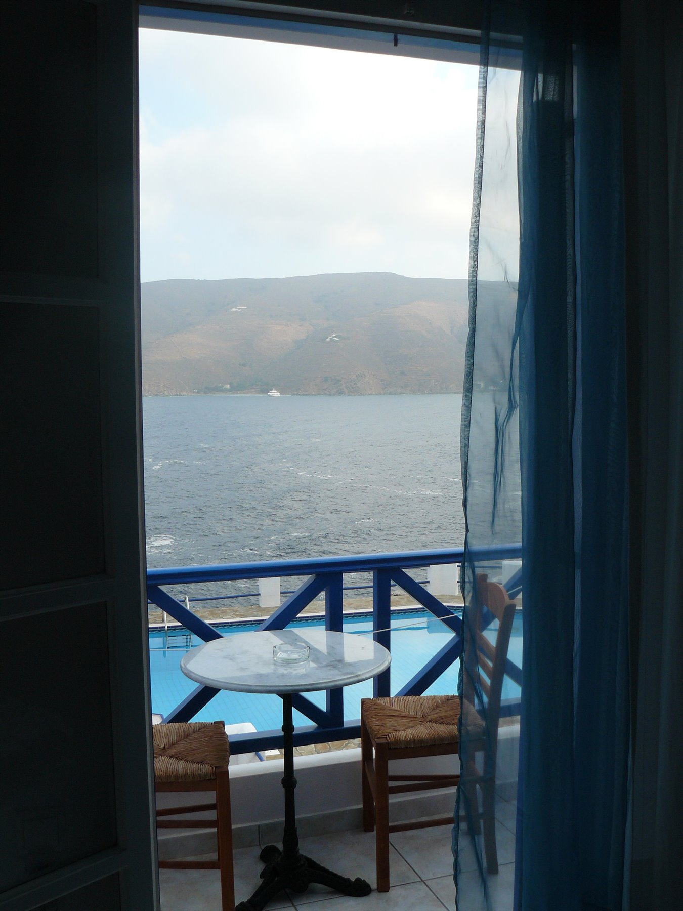 Tavolo con due sedie di paglia su balcone azzurro davanti al mare