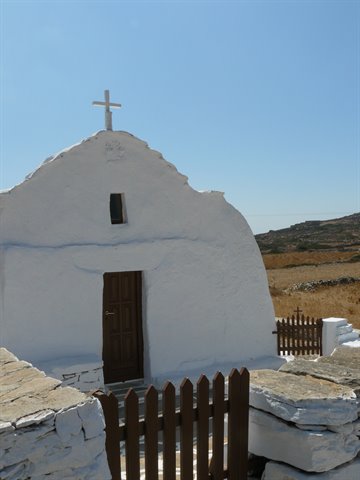 White chapel with cross, wooden fence and stone walls in Ios