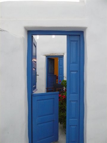 Blue half-open wooden door in whitewashed wall, red flowers behind