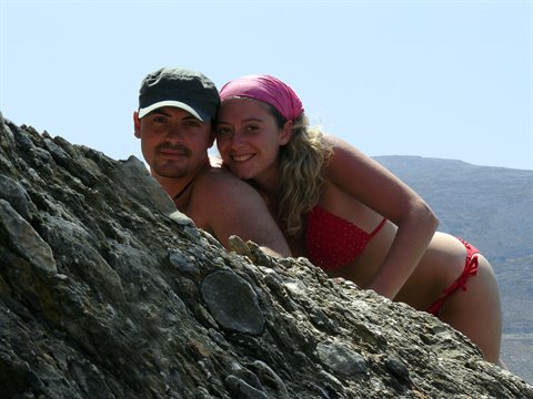 Couple in swimwear leaning on dark rock, arid mountains and blue sky behind