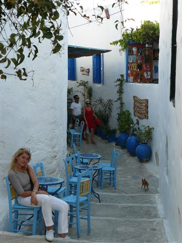 Woman sitting among blue taverna chairs in a whitewashed Cycladic alley