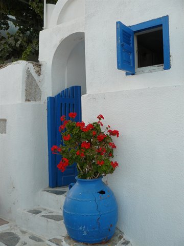 Whitewashed house with blue door and window, red geraniums in blue pot