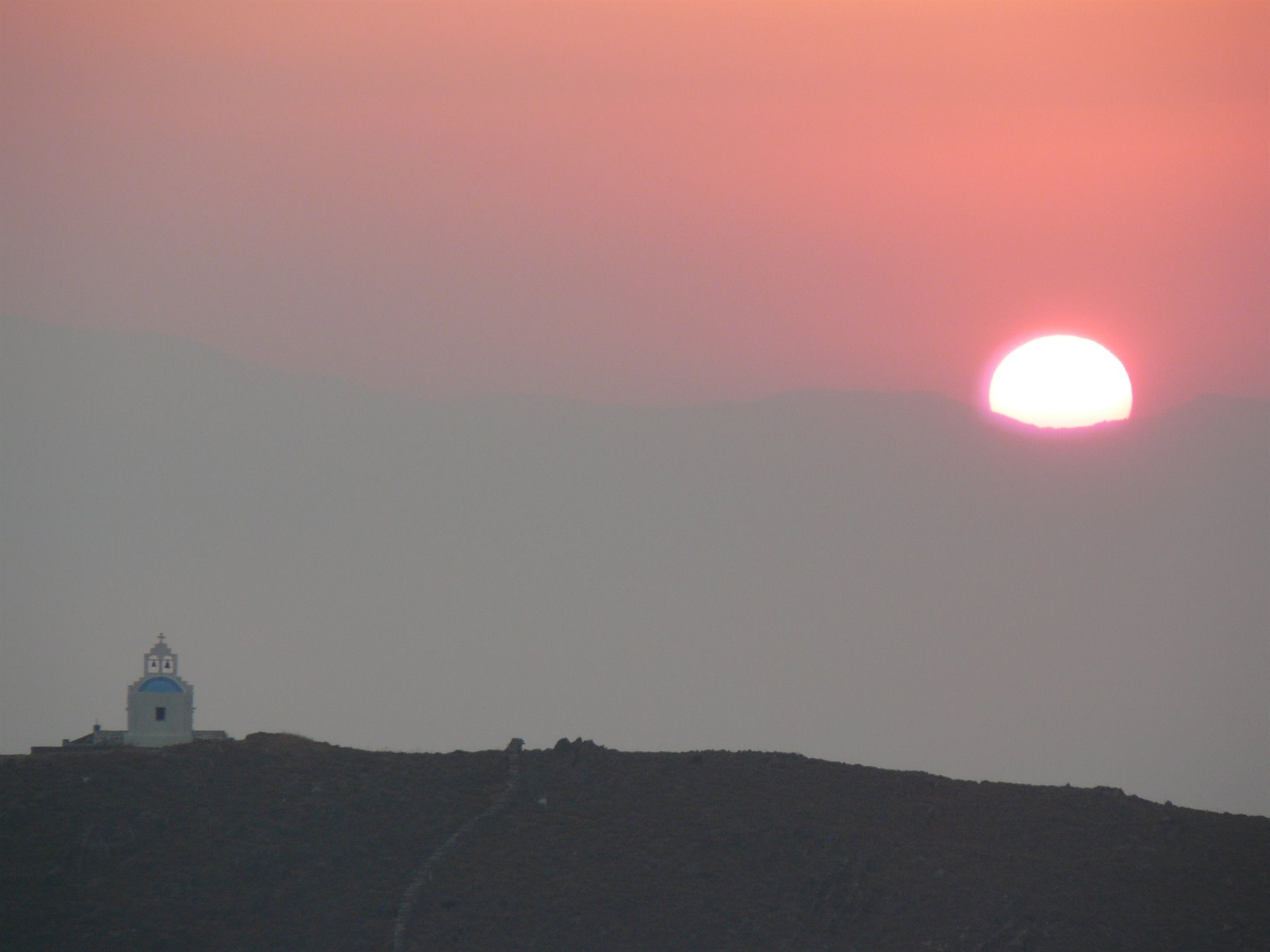 Sole rosso alba su collina scura, piccola chiesa bianca con campanile