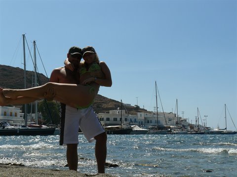 Man lifting a woman in a bikini on the beach, sailboats in the harbor
