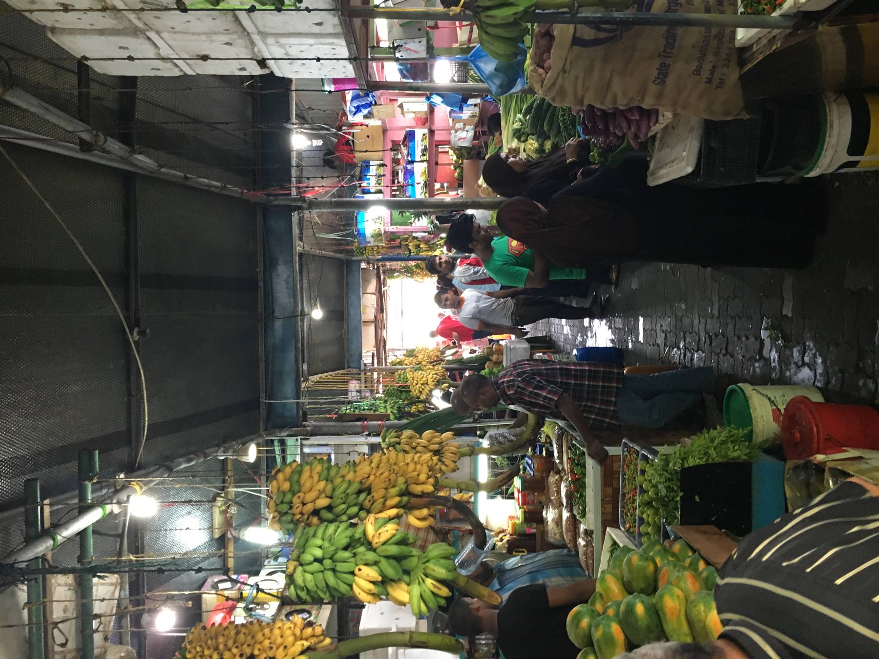 Mercato coperto con banchi di banane e papaye, gente che cammina tra gli stessi