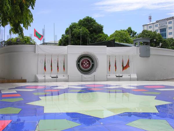 White monument with flags in Malé, colorful mosaic tile plaza reflecting sunlight