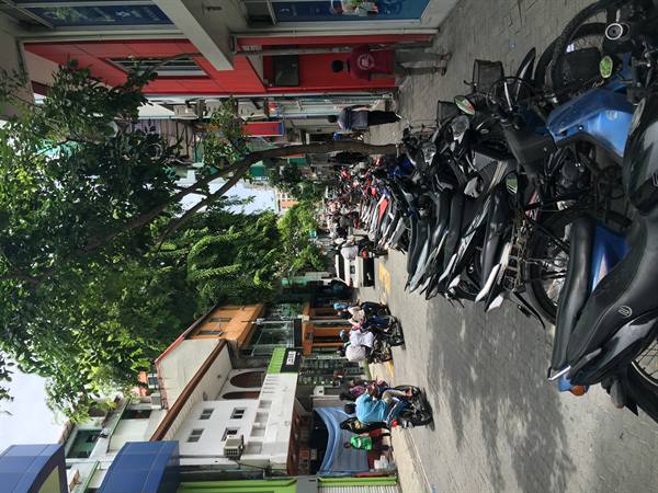 Motorbikes lined up on the sidewalk in front of shops, people walking