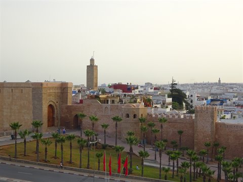 Mura rosse con porta e minareto a Rabat, palme e bandiere
