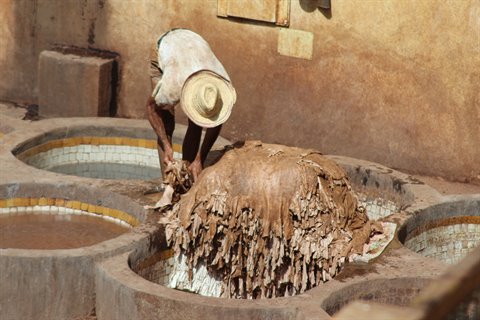 Artigiano col cappello di paglia lavora le pelli nelle concerie di Fes