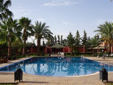 Blue pool surrounded by palms and black lanterns at a Marrakech resort
