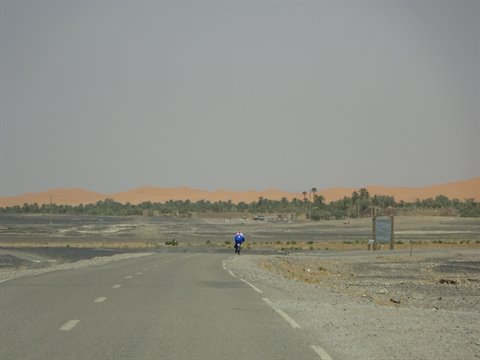 Ciclista solitario sull'asfalto verso le dune vicino a Merzouga