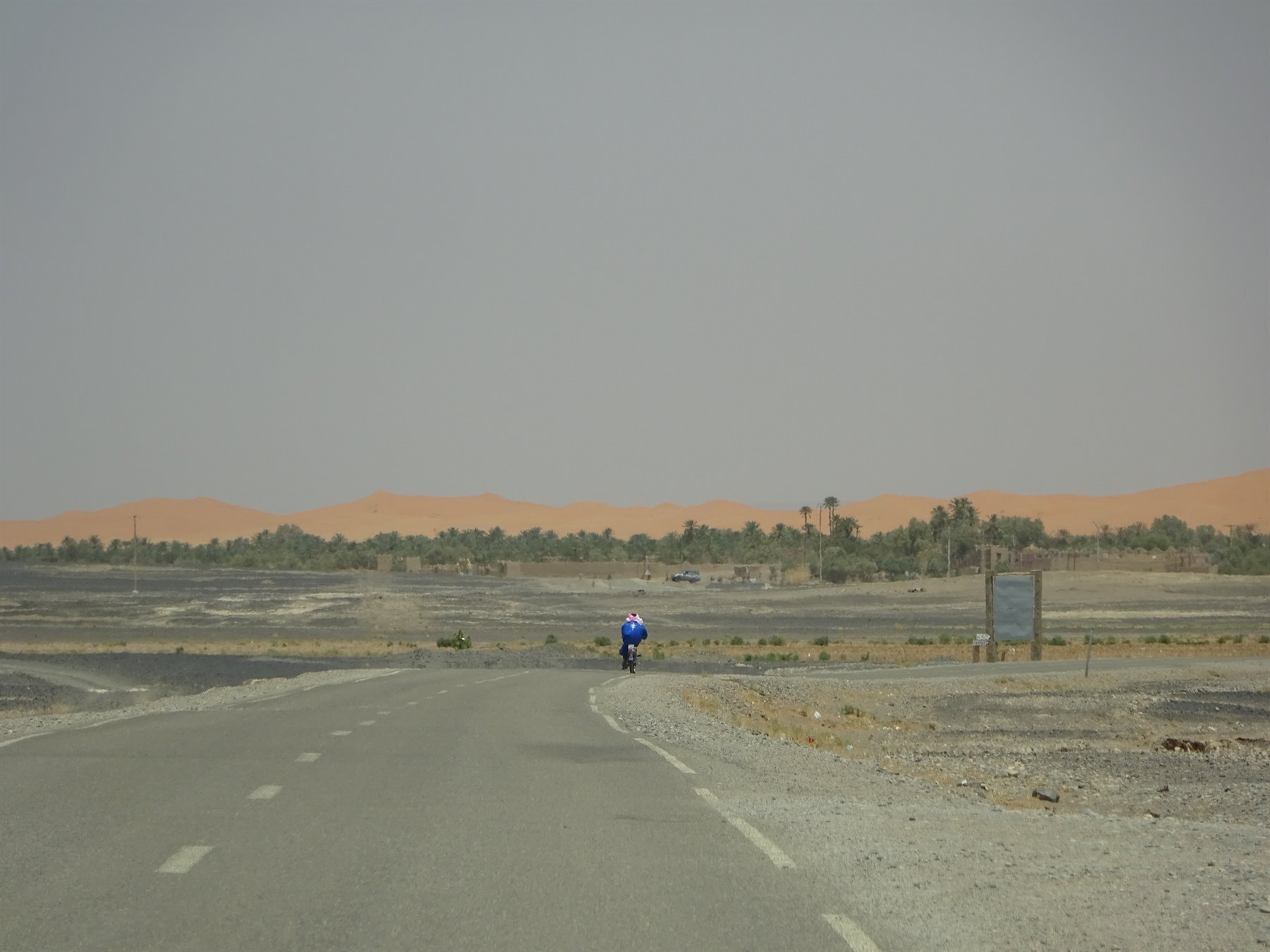 Ciclista solitario sull'asfalto verso le dune vicino a Merzouga