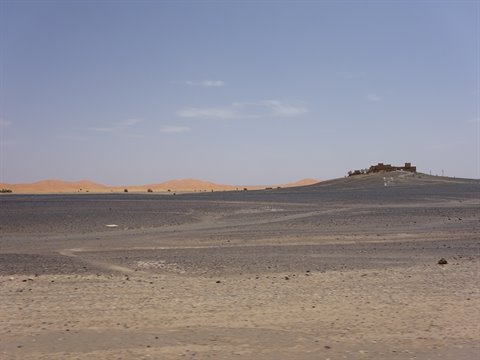 Kasbah in mattoni di terra su collina rocciosa, dune sabbiose a Merzouga