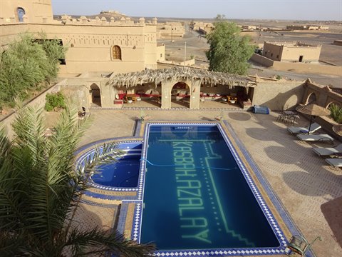 Piscina blu del Kasbah Azalay incorniciata da palme e muri di terra