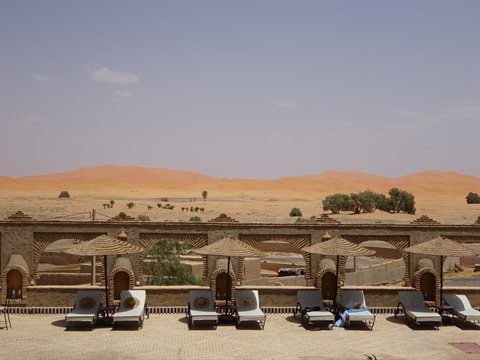 Terrazza con ombrelloni di paglia davanti alle dune di Merzouga