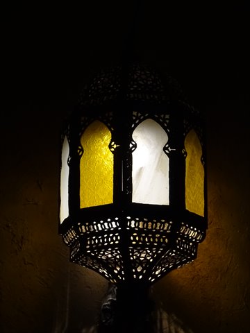 Lanterna in metallo traforato e vetro giallo illumina il muro scuro