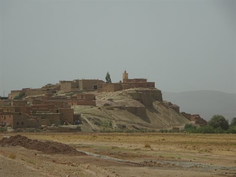 Mud-brick village on arid hill, minaret under hazy sky