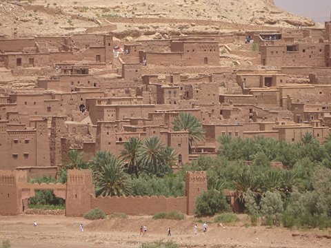 Earthen village against the hillside, palm trees, walls and walking people, Ait Ben Haddou