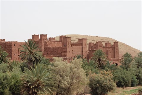 Red clay kasbah of Ait Ben Haddou among palms and hill