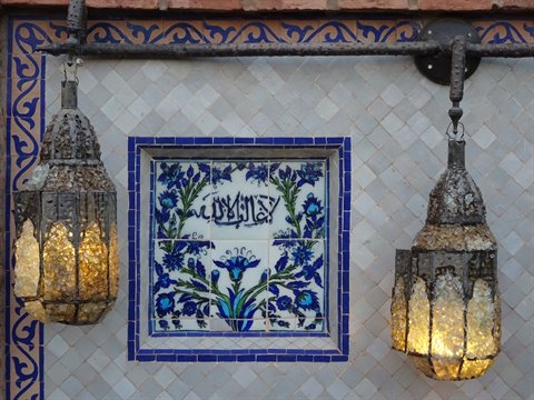 Pierced metal lanterns glow beside a blue floral tile with Arabic calligraphy, Marrakech